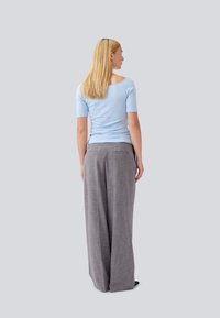 Lichtblauw top met korte mouwen en open rugontwerp, gecombineerd met hoge taille, wijde grijze broek met een subtiel ruitpatroon.