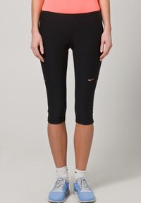 Czarne legginsy capri wykonane z elastycznego materiału, z dopasowanym krojem oraz małym różowym logo Nike na dolnej części nogi.