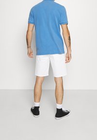Polo shirt bleu à manches courtes, shorts blancs, baskets montantes noires et chaussettes blanches. Tissu lisse sans motifs ni accents visibles.