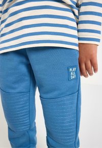 Niebieskie bawełniane spodnie dresowe z teksturowanymi panelami na kolanach i metką "PLAY ALL DAY". Połączone z koszulką w paski z długim rękawem.