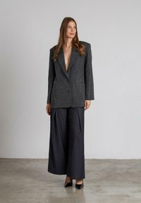 Blazer gris texturizado con un profundo escote en V, cierre de un solo botón y mangas anchas, combinado con pantalones de pierna ancha negros y tacones.