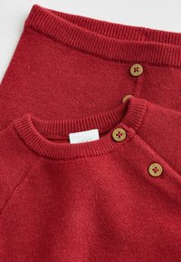 Red knit sweater and skirt set with ribbed necklines. Features two golden buttons with red centers. Soft texture and a casual design.