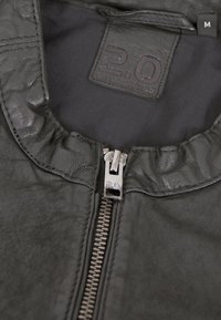 Schwarze Lederjacke mit Reißverschluss vorne, rundem Kragen und strukturierter Oberfläche. Das Innenetikett trägt die Aufschrift "2.0" mit der Größe "M."
