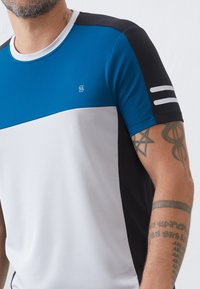 Kortermet sportsskjorte med et blått, hvitt og svart fargeblokkdesign, teksturert finish og hvite striper på ermene.