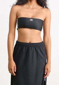 Černý bandeau top s bílým logem, doplněný černými kalhotami s vysokým pasem, zipy a elastickým pasem, s hladkou texturou.