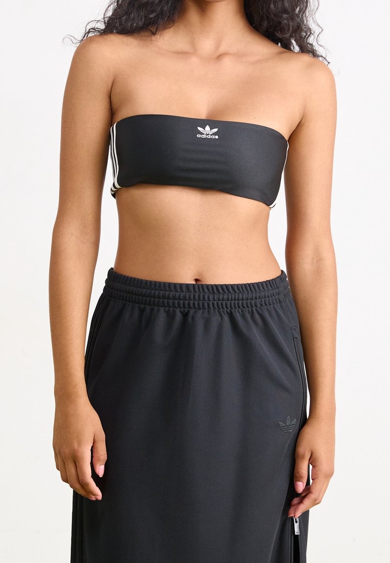 Černý bandeau top s bílým logem, doplněný černými kalhotami s vysokým pasem, zipy a elastickým pasem, s hladkou texturou.