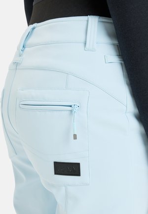 Helle blaue Hose aus glattem Material, mit einer Reißverschlusstasche und einem schwarzen Logo-Patch. Das Design umfasst taillierte Nähte und Gürtelschlaufen.