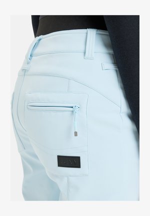 Lichtblauwe broek van gladde stof, met een gesloten zak en een zwart logo patch. Het ontwerp bevat nette stiksels en riemlussen.