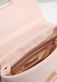 Světle růžová kabelka s texturovaným povrchem, zlatými kovovými doplňky a prostorným vnitřkem s látkovou podšívkou a značkovou etiketu.