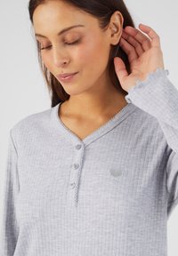 Top grigio a maniche lunghe con texture a coste, chiusura con bottoni, scollatura ondulata e piccolo graphic a forma di cuore. Tessuto morbido e vestibilità rilassata.