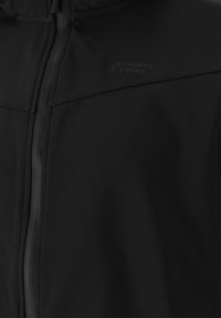 Sort softshell-jakke med lynlås foran, tekstureret stof og præget logo-detalje nær halslinjen.