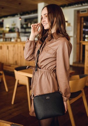 Braun faux Lederkleid mit langen Ärmeln und Gürtelakzent, kombiniert mit einer kleinen schwarzen Umhängetasche mit Reißverschluss und Kettenriemen.