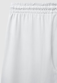 Weiße, weich strukturierte Sweatpants mit einem elastischen Taillenbund und gerafften Details. Der Stoff wirkt glatt und leicht.