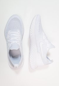 Baskets de sport blanches avec un dessus en mesh respirant, fermeture à lacets et semelle texturée. Présente une finition lisse et un détail de logo discret.