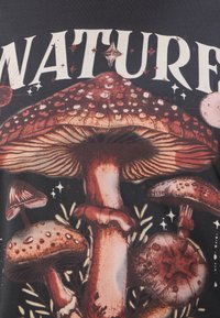 Chemise noire avec un motif de champignon vibrant dans des tons terreux, avec des détails texturés et le texte "NATURE" en lettres blanches en gras.