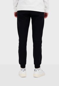 Svarta sweatpants med en smal passform, tillverkade av mjukt bomullsmaterial. Har ribbade muddar och ett elastiskt midjeband. Bärs tillsammans med vita sneakers.
