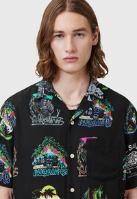 Camisa negra de manga corta con estampados gráficos coloridos de animales y follaje, con un bolsillo en el pecho y un corte relajado. Textura satinada.