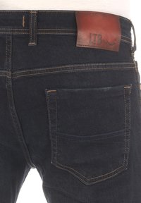 Jean en denim foncé avec un patch en cuir marron portant l'étiquette "LTB", avec des coutures orange et un détail de poche arrière.