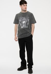 Gray graphic t-shirt featuring a skull and wings design, paired with black trousers and black boots. Simple, casual fit with short sleeves.