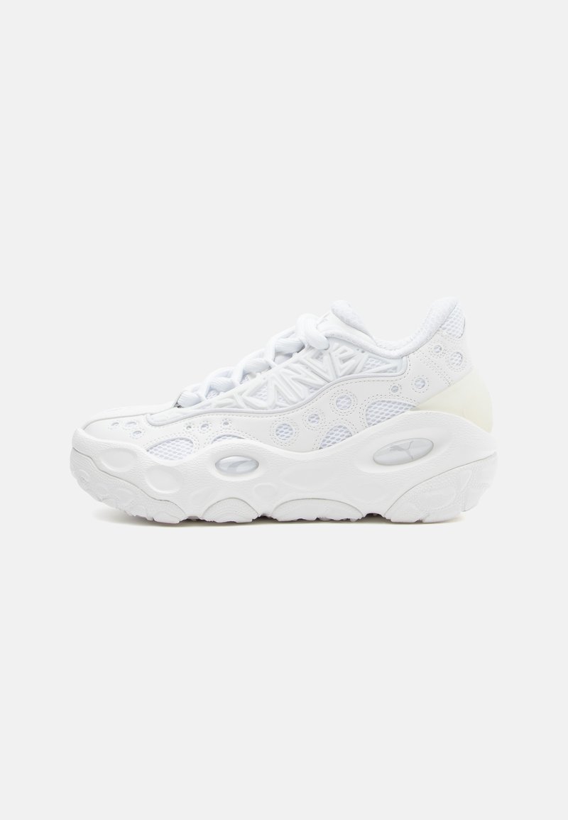 Baskets de sport blanches avec une tige en mesh texturé, bout arrondi et semelle épaisse avec des découpes circulaires pour la ventilation.