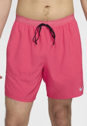 Mężczyzna noszący jasnoróżowe spodenki do biegania Nike z czarnym sznurkiem i odblaskowym logo Nike na lewej nodze.