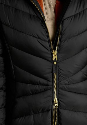 Czarna kurtka puchowa z pikowanym wzorem, z złotymi zapięciami i kontrastującymi teksturami. Kołnierz jest nałożony na spodzie.