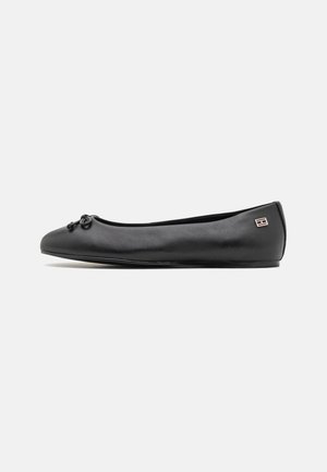 Schwarzer Leder-Ballerinaschuh mit einer kleinen Schleife auf der Schuhspitze und einem metallischen Logo in der Nähe der Ferse, seitlich dargestellt.