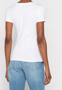 Biała koszulka z krótkim rękawem, wykonana z bawełny, z okrągłym dekoltem i dopasowanym krojem. Tył ma gładką, nieozdobioną powierzchnię.