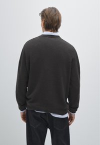 Czarny sweter w ciemnoszarym kolorze, wykonany z miękkiego materiału, o luźnym kroju, okrągłym dekolcie i prążkowanym wykończeniu; noszony na białej koszuli z kołnierzykiem i ciemnych dżinsach.