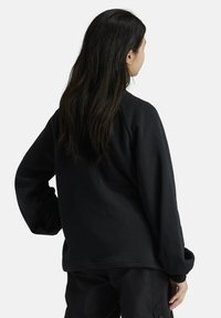 Sudadera negra de manga larga, cuello redondo y hombros caídos. Tejido suave de mezcla de algodón con un ajuste relajado y sin patrones visibles.