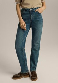 Niebieskie jeansy z wysokim stanem wykonane z denimu, prosty fason nogawki z minimalnymi przetarciami. Sparowane z brązowym obuwiem sznurowanym na grubej podeszwie.