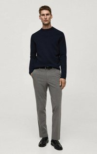 Mornarski pleteni pulover s okruglim izrezom, uparen s laganim sivo-zelenim krojenim hlačama i crnim kožnim cipelama, stoji protiv neutralne pozadine.