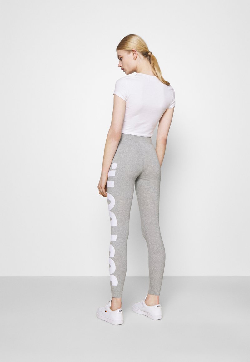 Leggings grises con texto en blanco que dice "sport" a lo largo de la pierna izquierda, combinados con una camiseta ajustada de manga corta blanca y zapatillas blancas.