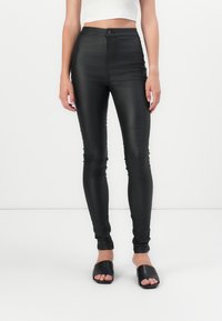 Svarta högmidjade leggings med glansig yta, åtsittande design och slät textur, parat med svarta öppna klackskor.