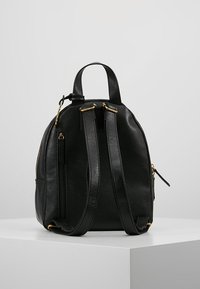 Schwarzer Leder-Rucksack mit runder Form, ausgestattet mit zwei Schulterriemen, goldfarbenen Hardware-Akzenten und einer seitlichen Reißverschlusstasche. Glatte Textur.