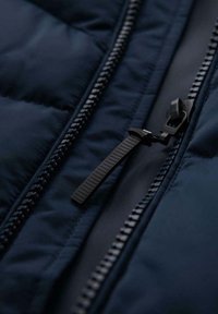 Giacca imbottita blu navy realizzata in tessuto con una zip ben visibile dotata di accessori neri e un tab di presa texturizzato, evidenziando un design trapuntato.