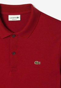 Rød polo t-shirt lavet af bomuld, med ribbet krave, to sorte knapper og et grønt krokodillelogo på venstre bryst. Regular fit.