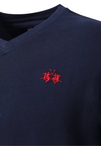 Camiseta azul marino con cuello en V y un pequeño logo bordado rojo que muestra a dos jugadores de polo a caballo cruzando sus mazos.