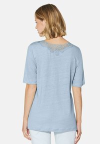 Lichtblauw T-shirt met korte mouwen en een kanten accent rond de halslijn. Zachte stoftextuur; casual pasvorm. Stikdetails zichtbaar bij de schouders.