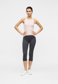 Débardeur rose clair avec un col rond, associé à des leggings courts gris foncé. La tenue est complétée par des baskets blanches.