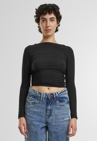 Crni dugosleeve crop top s glatkom teksturom i okruglim izrezom, u kombinaciji sa svijetloplavim trapericama visokog struka koje imaju istrošen detalj.