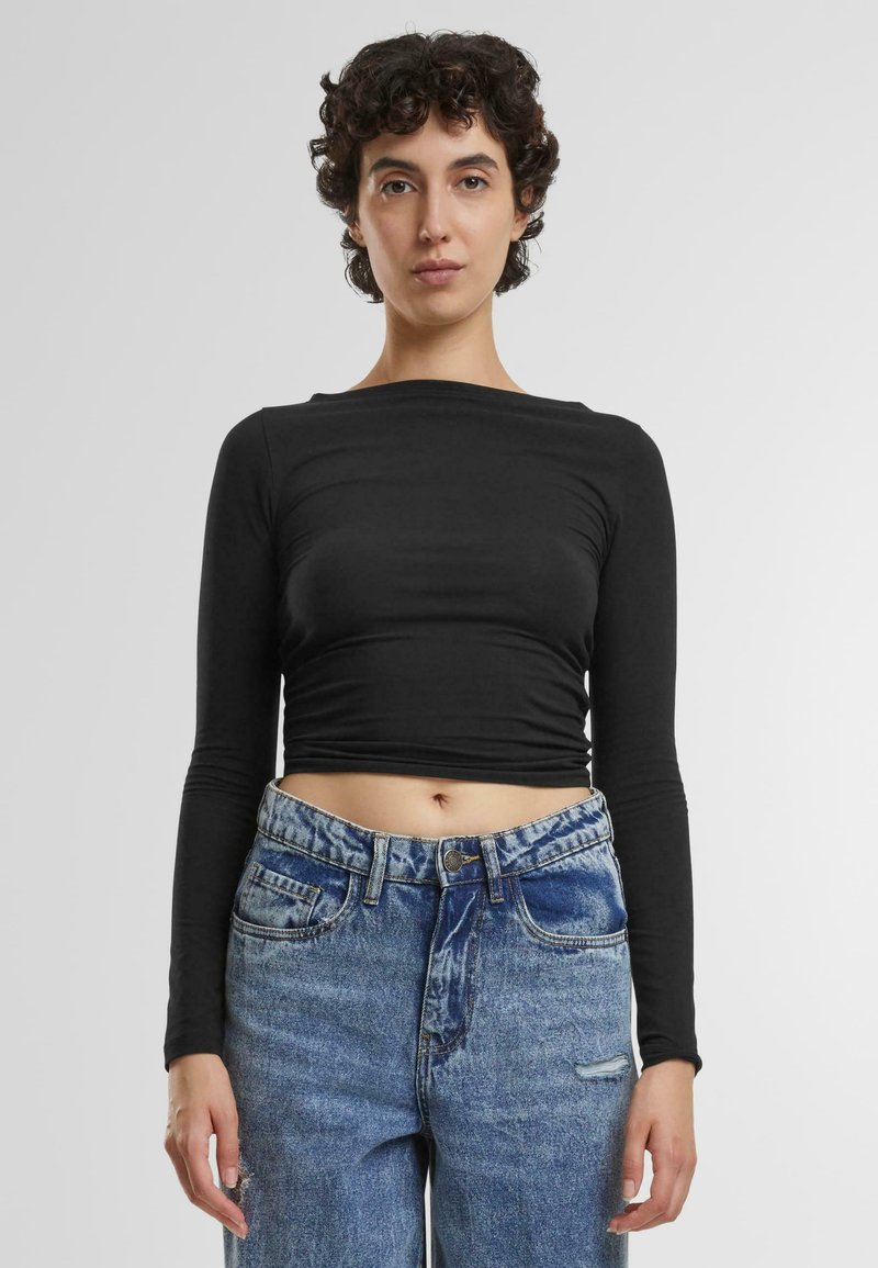 Crni dugosleeve crop top s glatkom teksturom i okruglim izrezom, u kombinaciji sa svijetloplavim trapericama visokog struka koje imaju istrošen detalj.