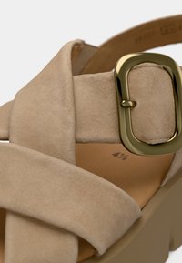 Beige suede sandal with crisscross straps, gold rectangular buckle, soft textured upper, and a chunky beige sole. Size marked inside.