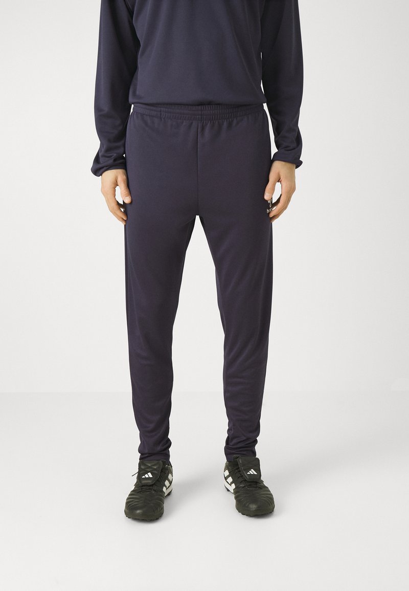 Marineblauwe sportbroeken met een elastische tailleband, slim fit, gladde textuur en taps toelopende benen, gecombineerd met zwarte voetbalschoenen met witte strepen.