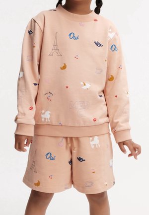 Niño con sudadera y pantalones cortos color melocotón con estampados temáticos franceses que incluyen la Torre Eiffel, cruasanes, pájaros y el texto "Oui".