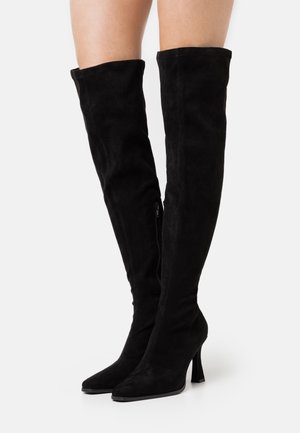 Bottes noires au-dessus du genou en daim doux, avec un bout pointu, un talon haut et fin, et une fermeture éclair latérale pour un enfilage facile.