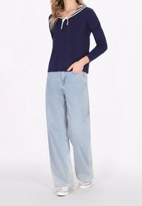 Námořnický pletený top s bílým pruhovaným límečkem a šňůrkou, doplněný světle modrými kalhotami s širokými nohavicemi. Obsahuje detaily knoflíků a volný střih.