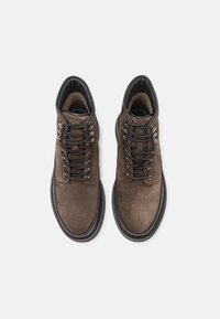 Stivali alla caviglia in suede marrone con suola nera. Presentano occhielli metallici e lacci piatti. Fodera interna liscia per un comfort ottimale.