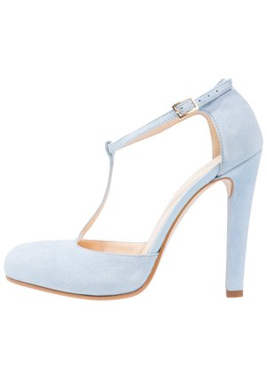 Chaussure à talon haut en daim bleu clair avec bride en T et boucle dorée, bout fermé et talon fin sur fond blanc.