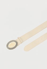 Ceinture en cuir beige avec boucle ovale en argent ornée d'un motif tourbillonnant crème et plusieurs trous de réglage sur fond blanc.